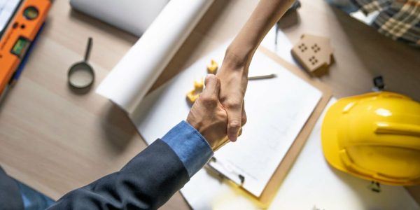 Architect or civil engineer and house owner shaking hands after house finish or discuss about home drawing on working site.